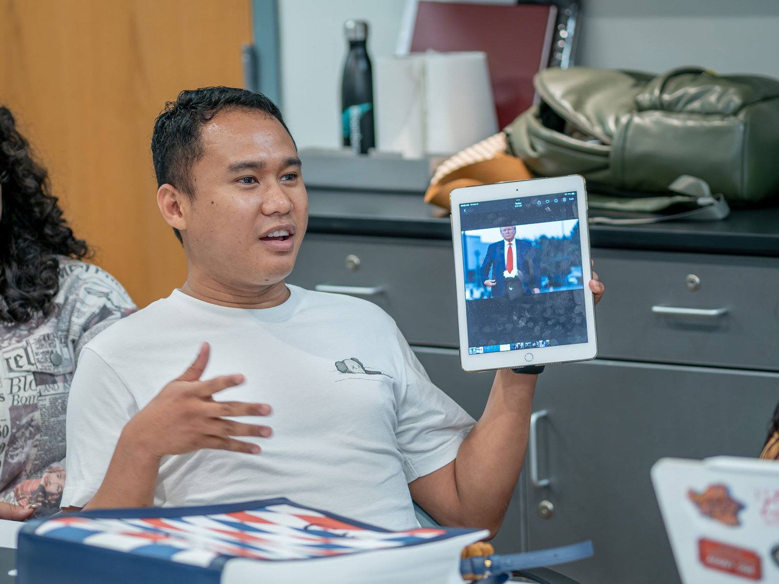 Student Nelson Dela Cruz holds a tablet with a manipulated image of Donald Trump in a shorter tie.