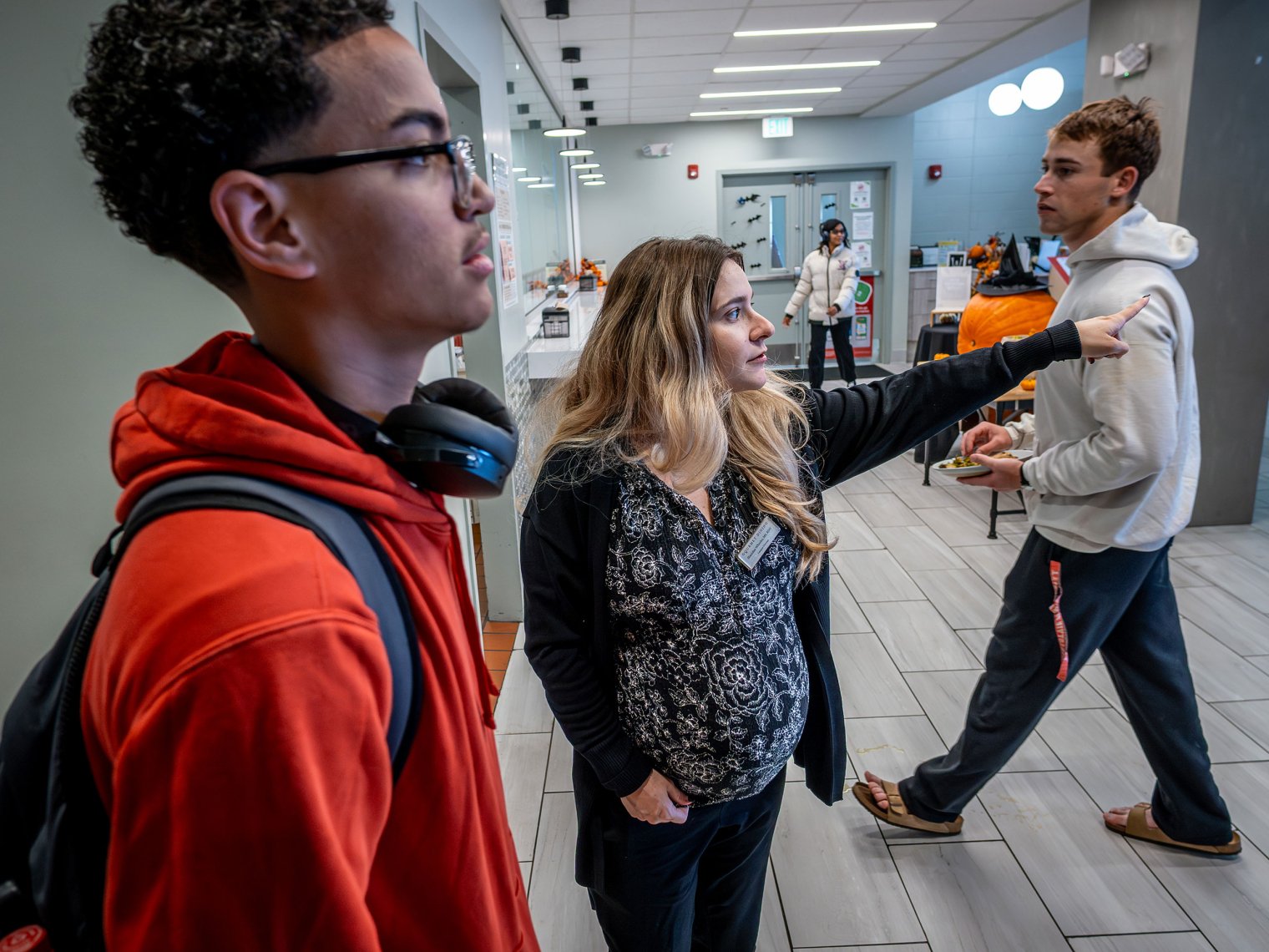 Woman with blonde hair pointing to the right and young man in a red sweater looking off in said direction. 