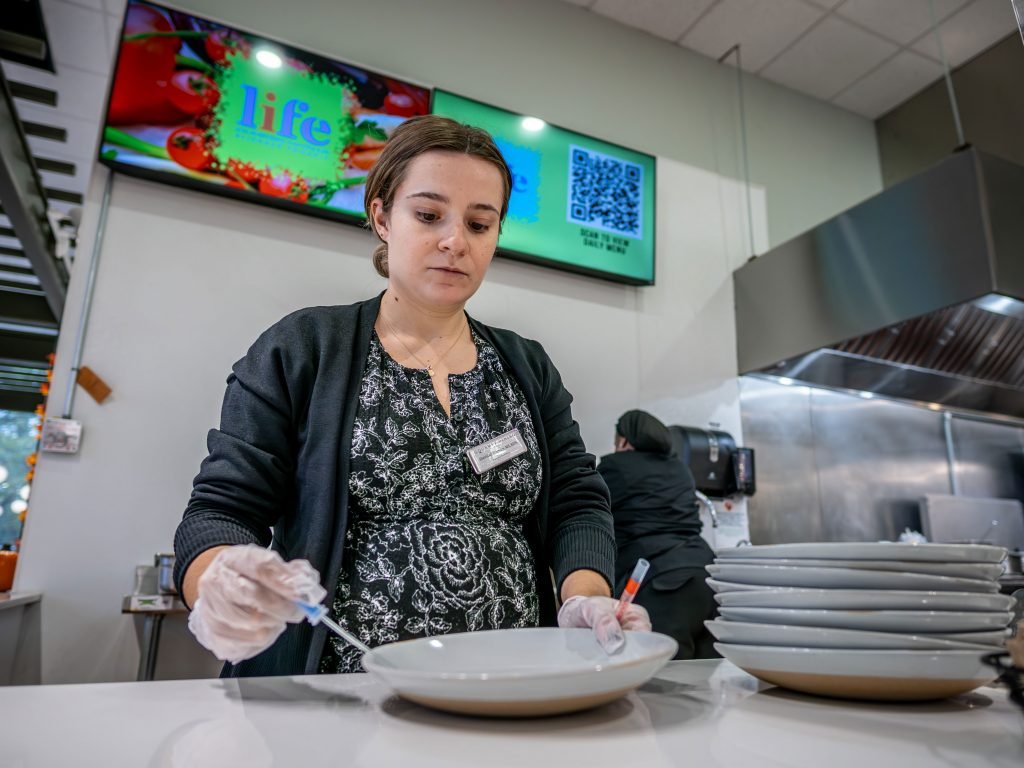 Woman swabbing dining plates with gloves on. 