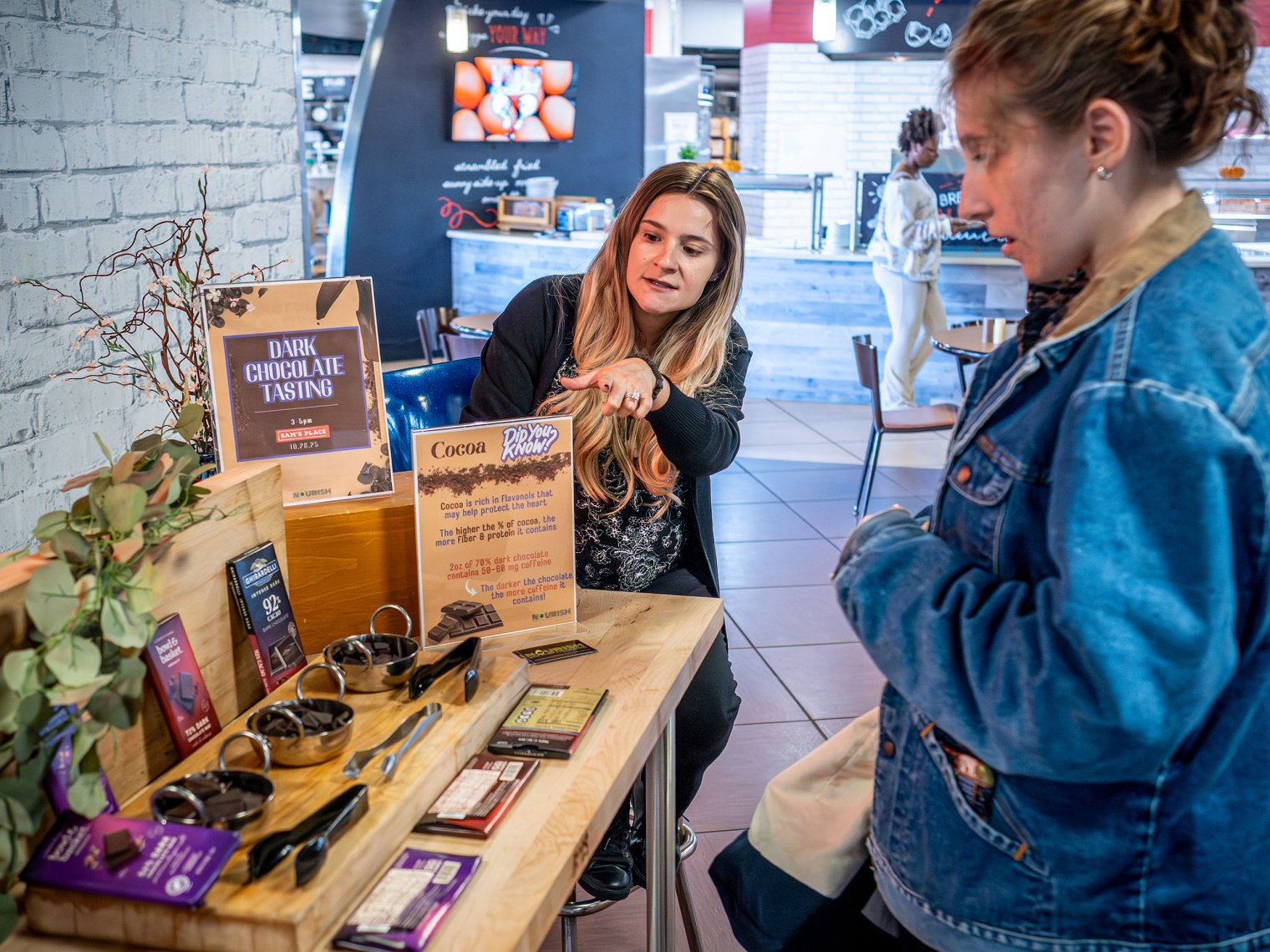 Women demonstrating her booth of chocolate to another woman. 