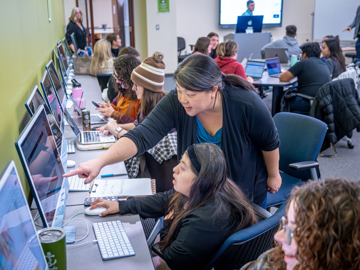 A professor points to a computer screen while helping a student.