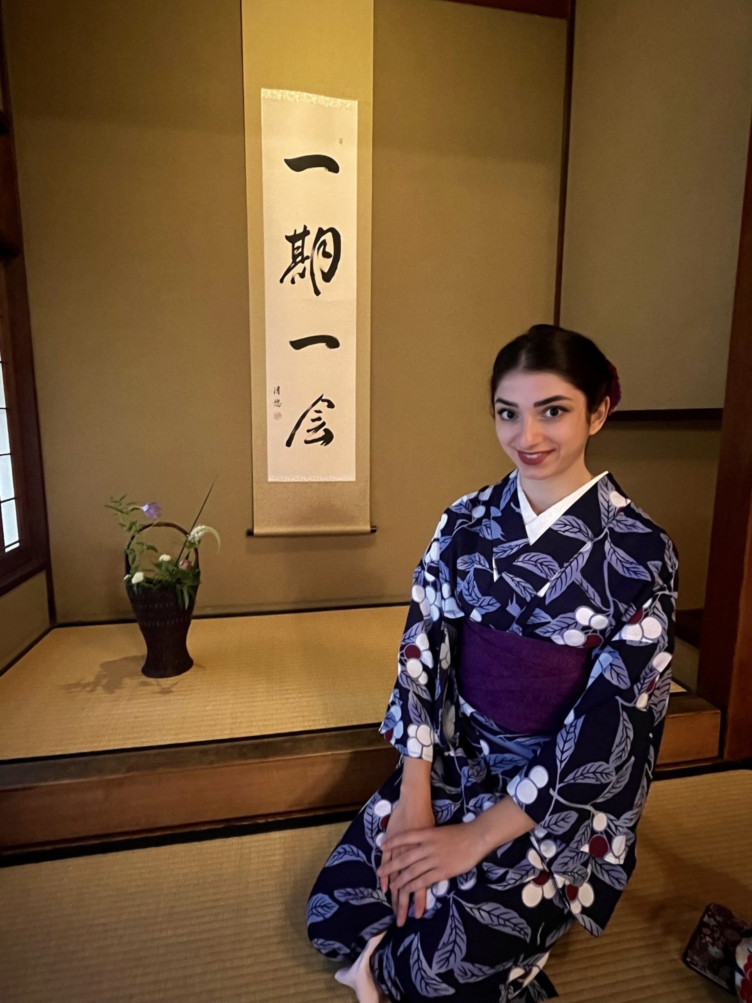 Melissa Spigelman, dressed in a traditional Japanese kimono, sits in a Japanese room with a scroll and flower arrangement in the background.