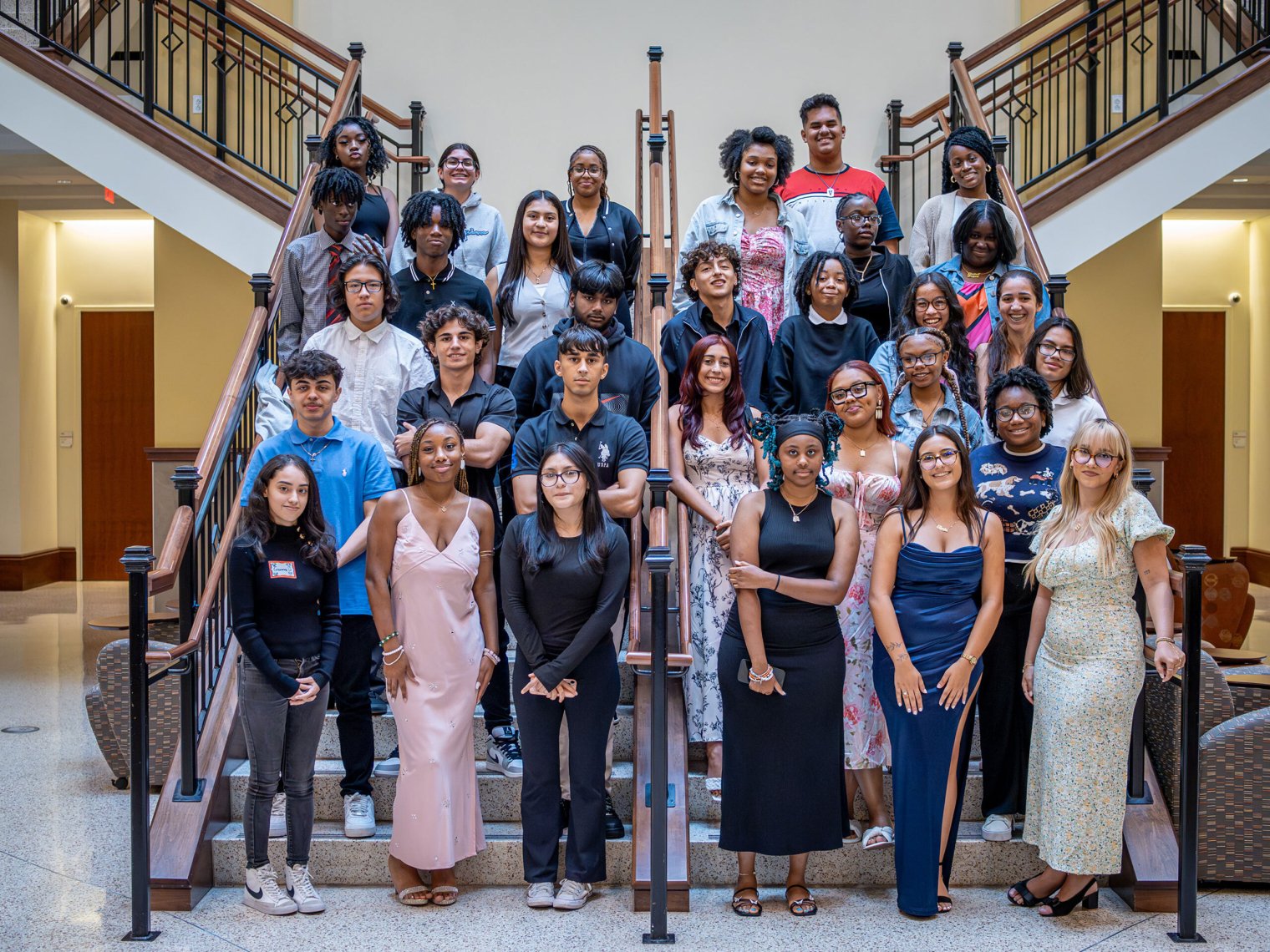 Group portrait of students from the Red Hawk Rising program posing on a staircase at Montclair State University. The students are dressed in a mix of formal and casual attire, smiling as they stand in rows on the staircase.