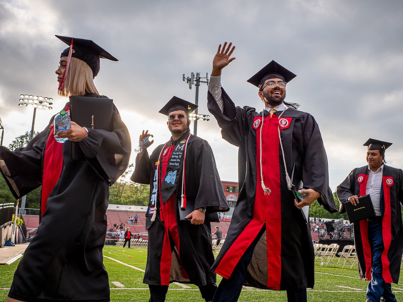 Group of graduates at commencement in black cap and gowns, waving.