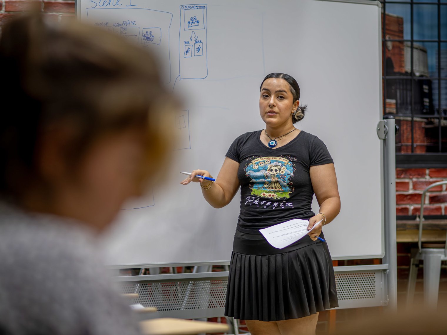 A student stands in front of a whiteboard and presents to the rest of the class