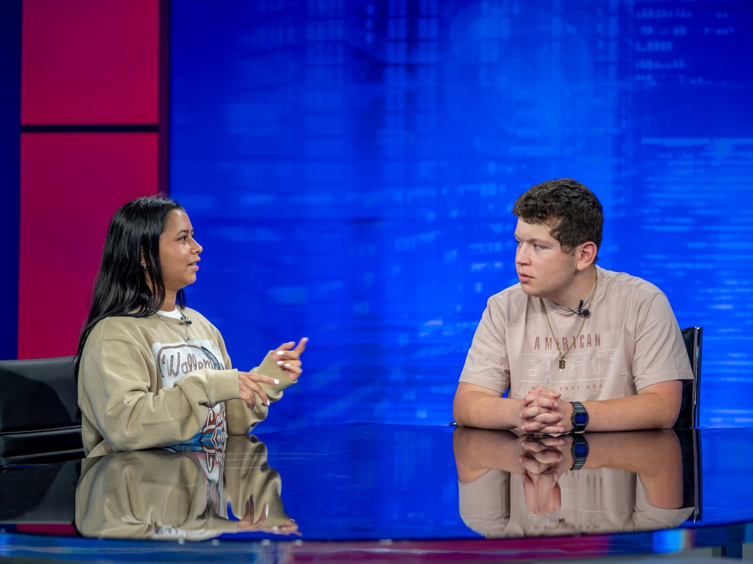 Two students converse on a TV news studio set