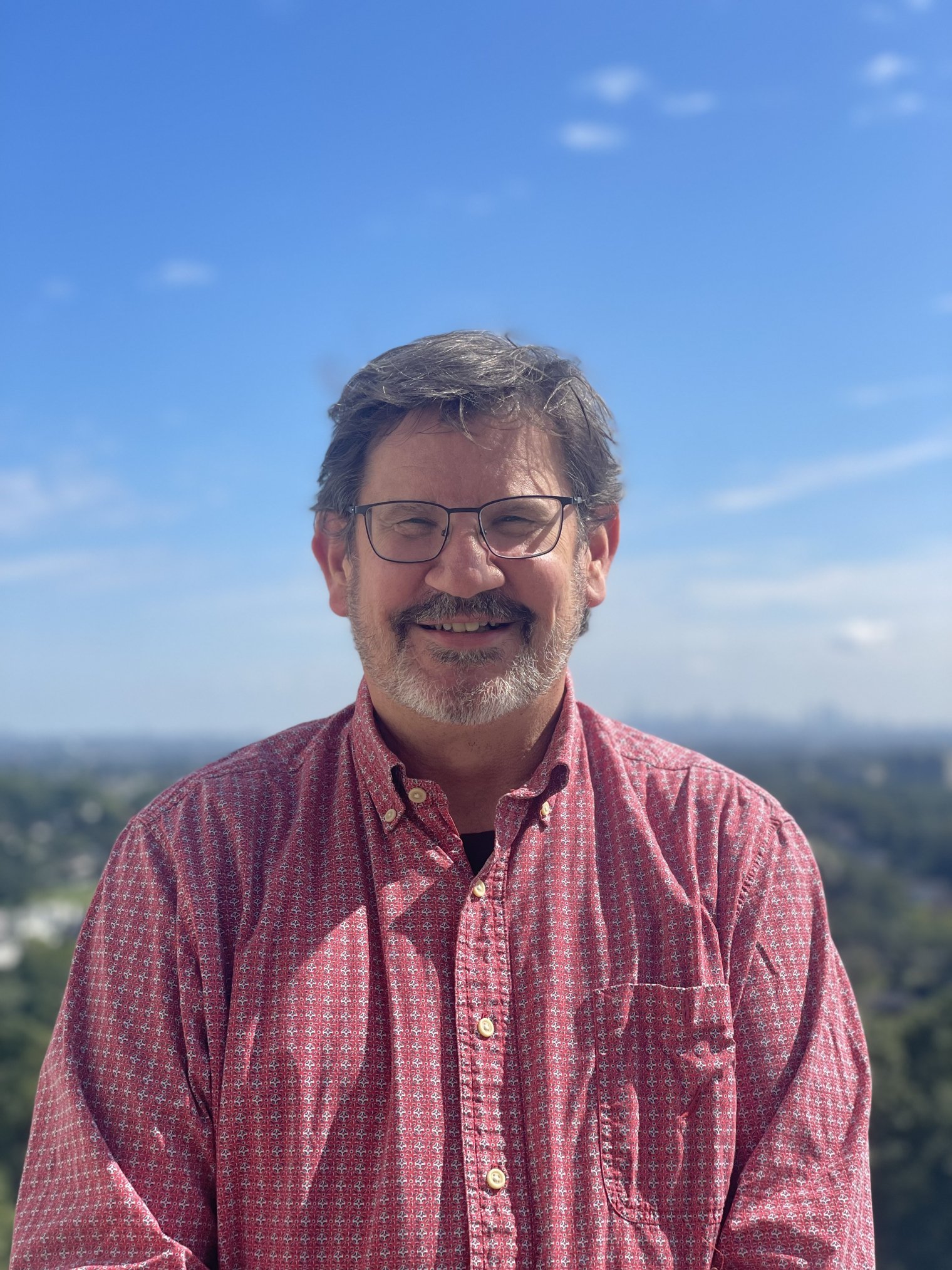 Greg Pope headshot smiling in glasses and a pink button down.