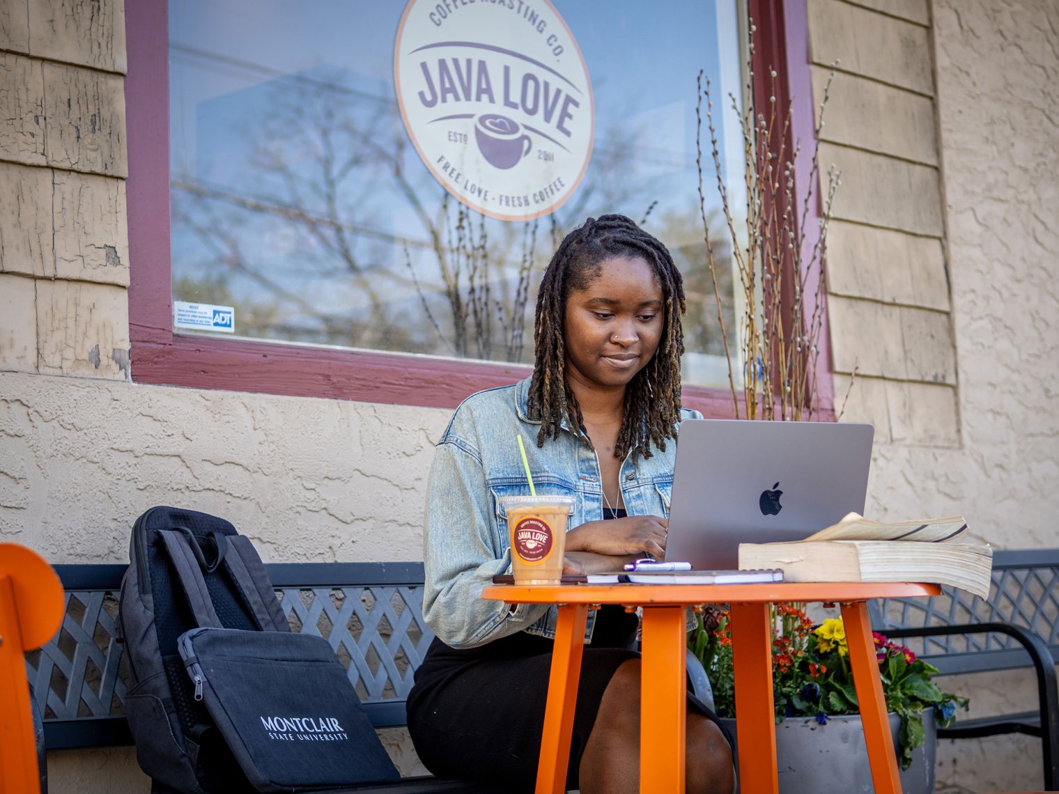 Student wearing jean jacket seated with laptop outside a cafe