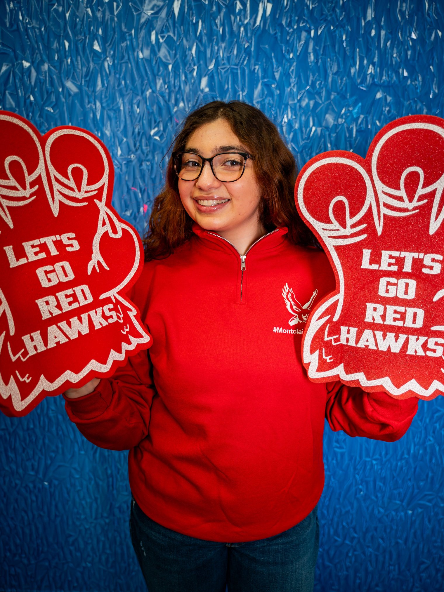 Photo of a woman in a red Montclair sweatshirt brandishing two foam talons that read Let's Go Red Hawks