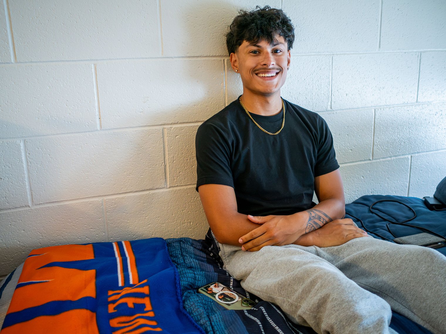 Dominic Lugo sits on his made bed. 