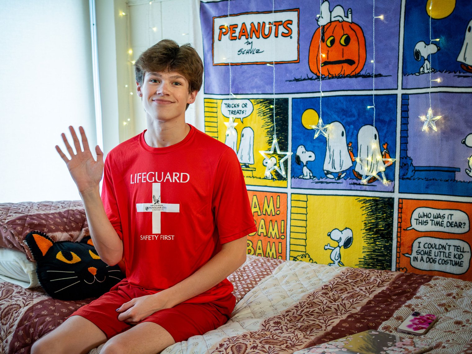 Jaxon Walsh wears his lifeguard t-shirt while sitting on his bed. 