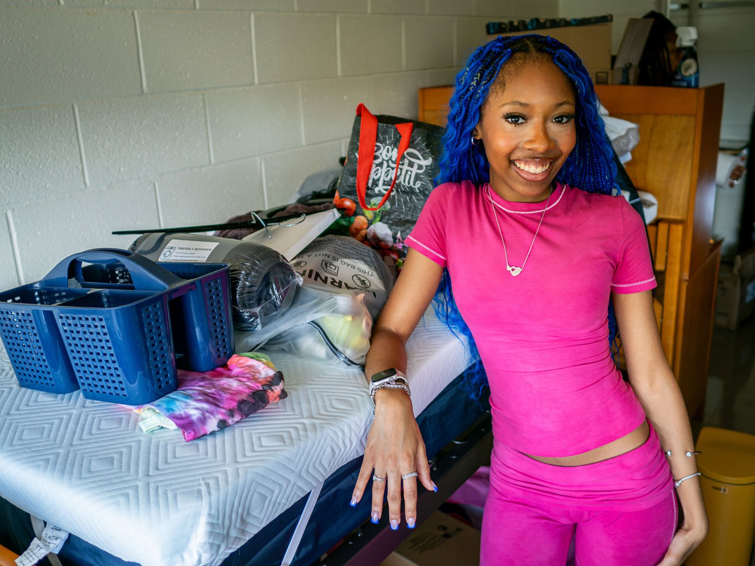 Mackenzie Plummer leans on her dorm bed loaded with her bedding and supplies.