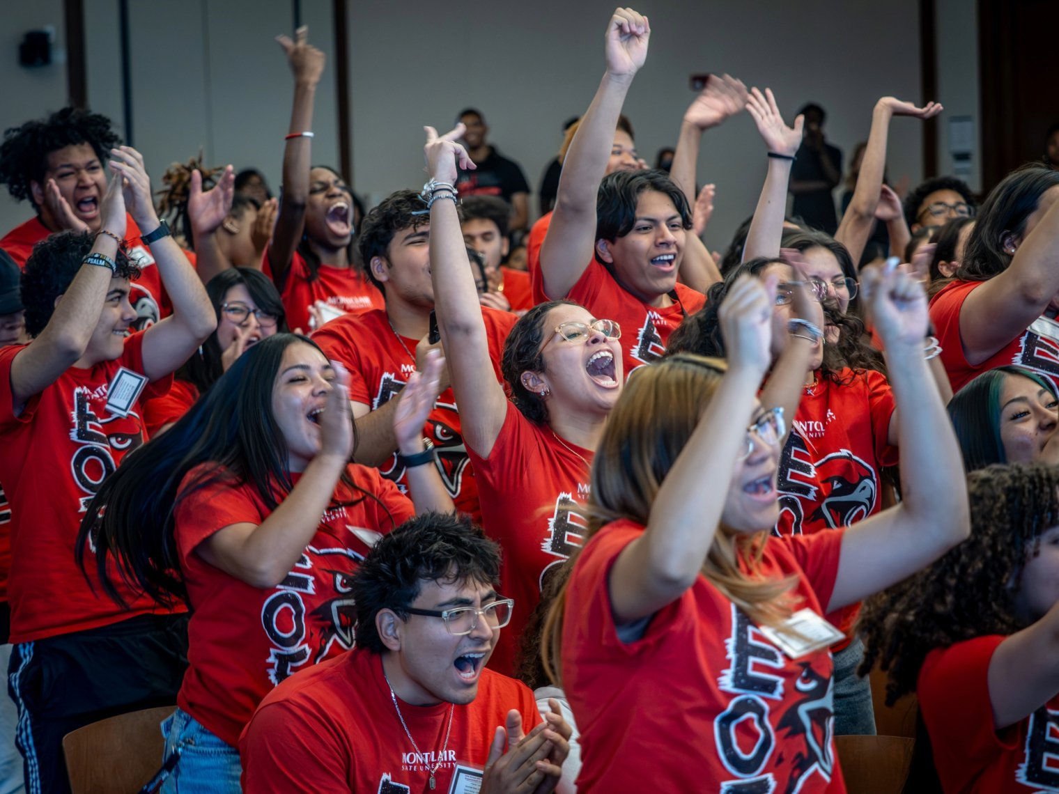 Close-up of students in red Montclair State EOF T-shirts raising their arms and cheering with mouths open in excitement.