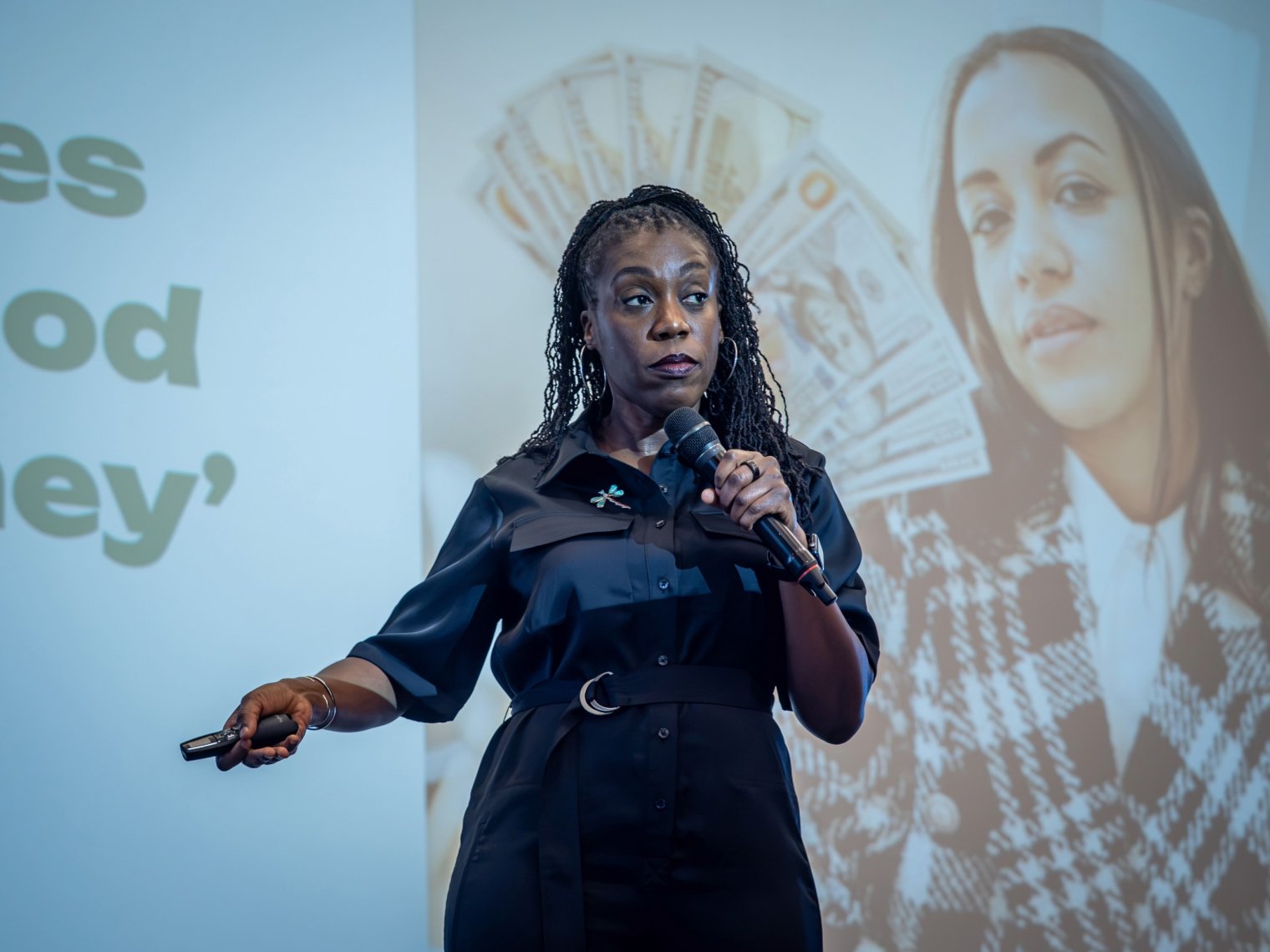 Keynote speaker Tiffany 'The Budgetnista' Aliche speaks into a microphone on stage, with an image of a hand holding cash projected on the screen behind her.