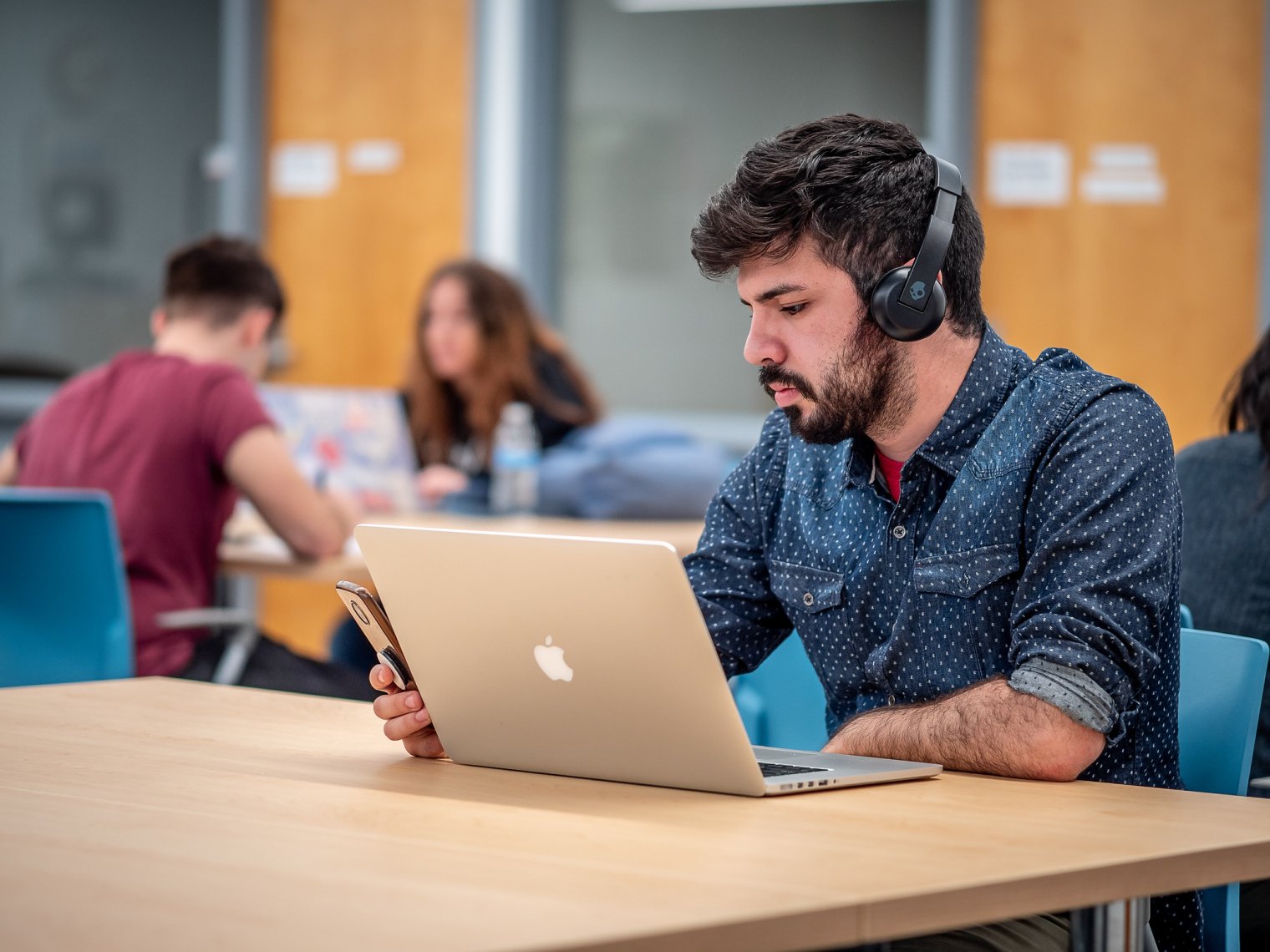 Male student in Sprague Library wearing headphones in front of his laptop.