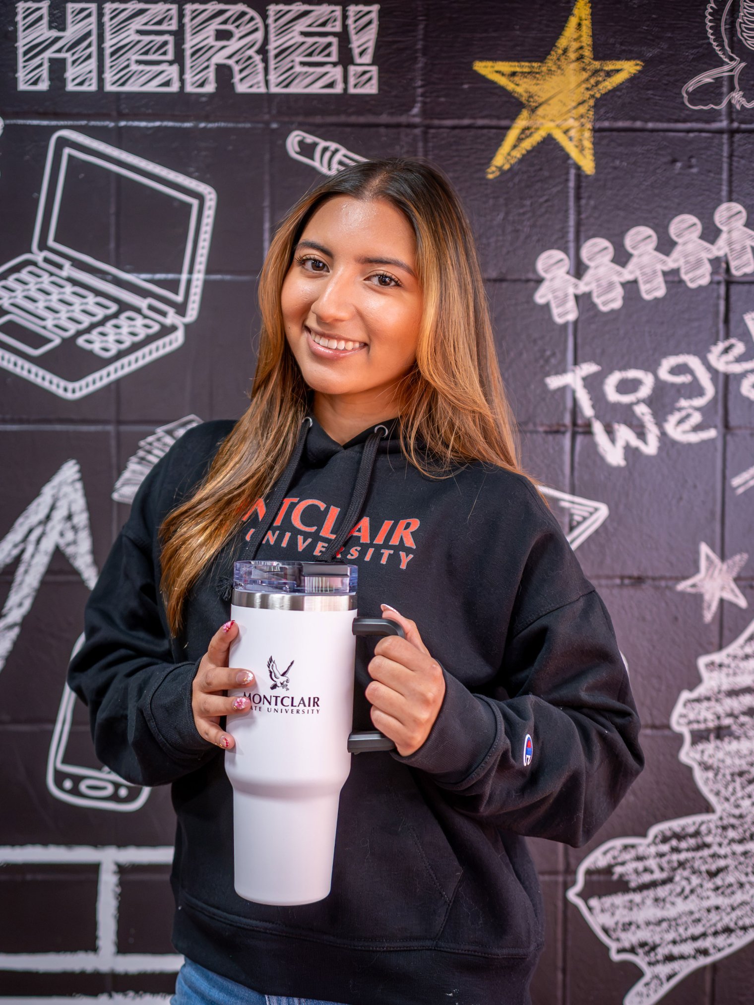Arianni Unigarro smiling at the camera, holding up a water bottle that says Montclair State Univeristy.