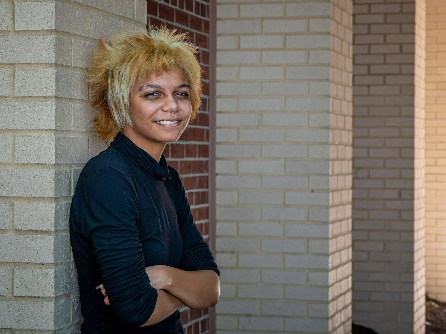 Student Aman Gregory leaning against brick pillar at Bloomfield College