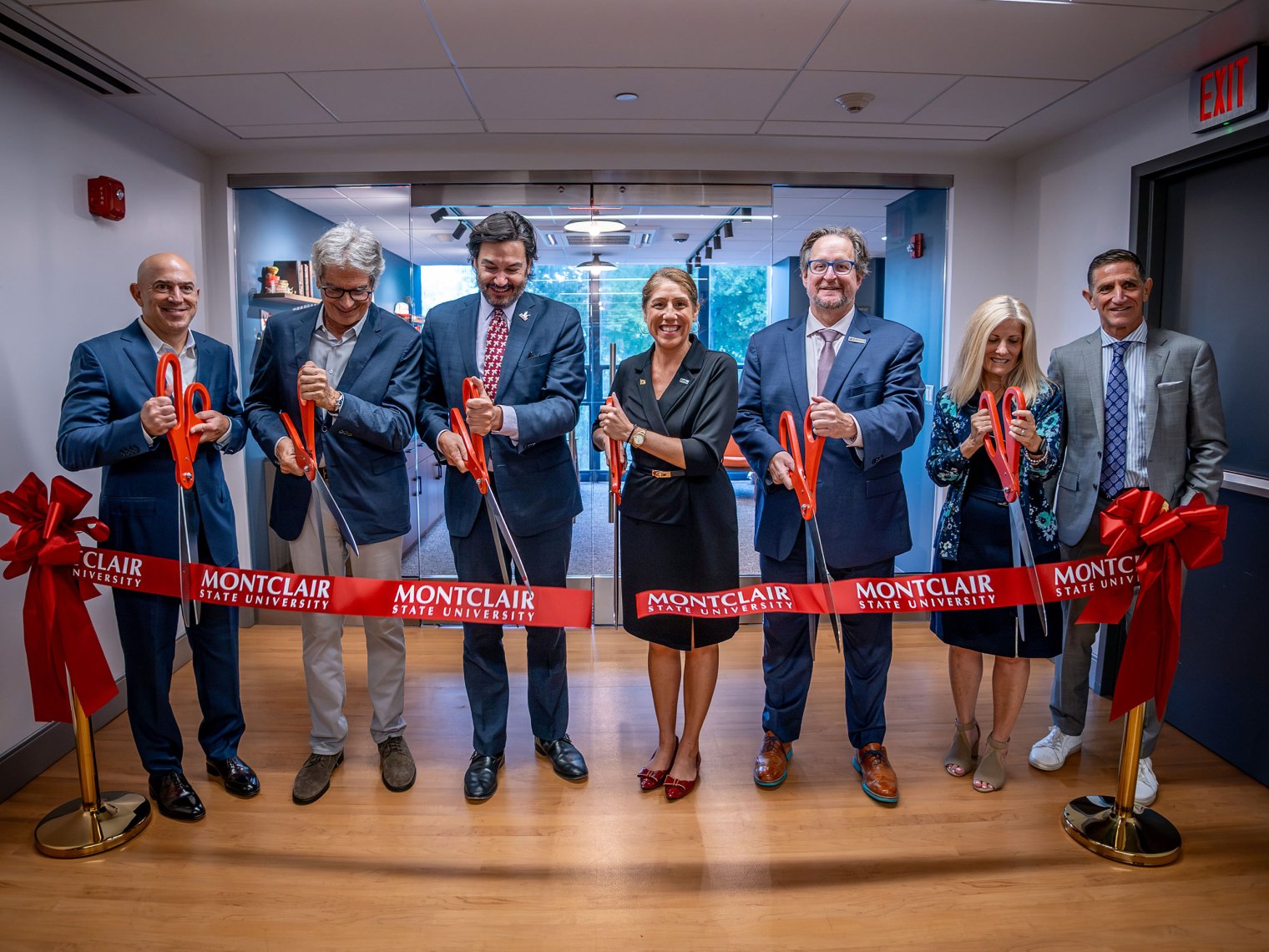 Seven people stand behind ceremonial ribbon with large scissors at the Dreamscape opening