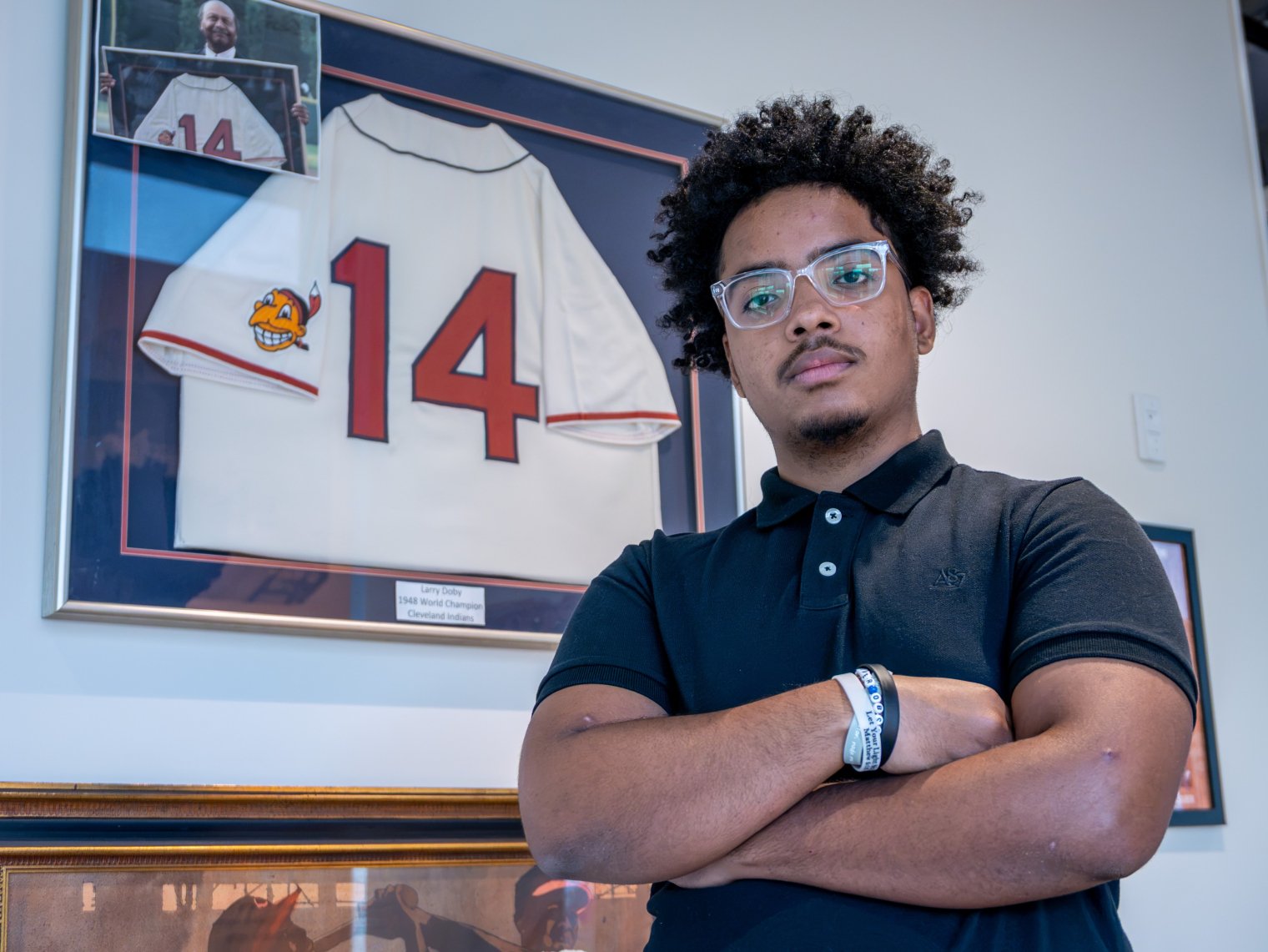 Edward Gonzalez stands with arms crossed by a baseball jersey with the number 14.