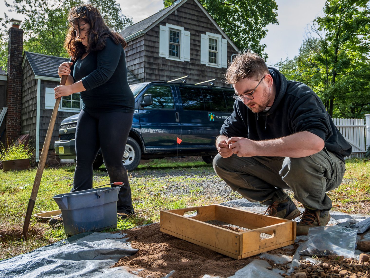 A student digs a hole with a shovel while another examines a soil sample.