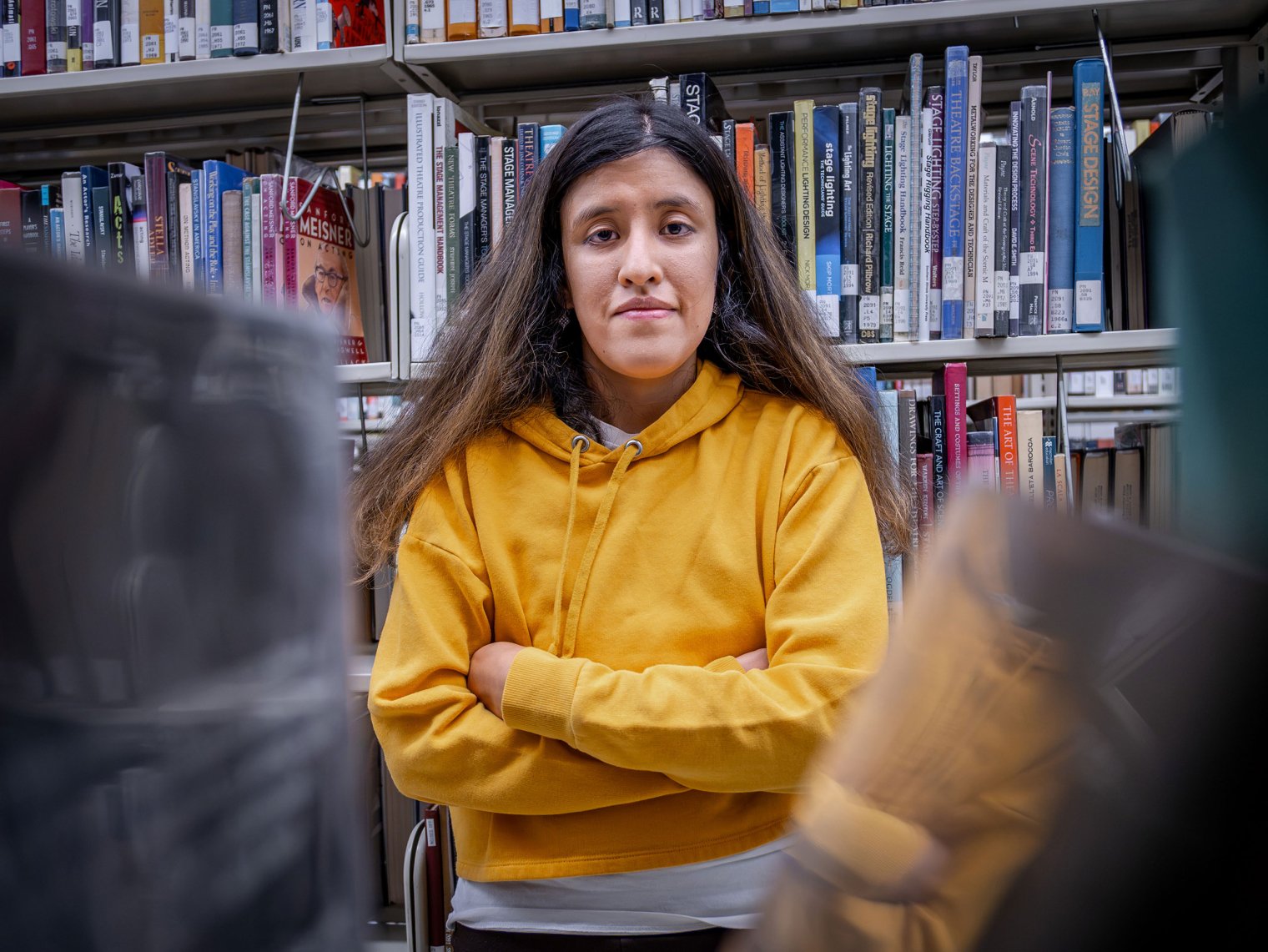Jessica Sucuzhanay stands with arms crossed in the library.