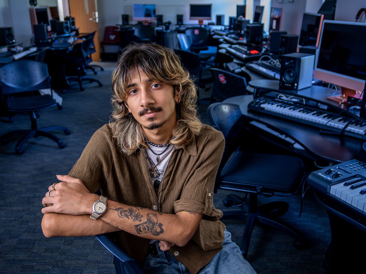 Nirmay Naik sits among keyboards in a music classroom.