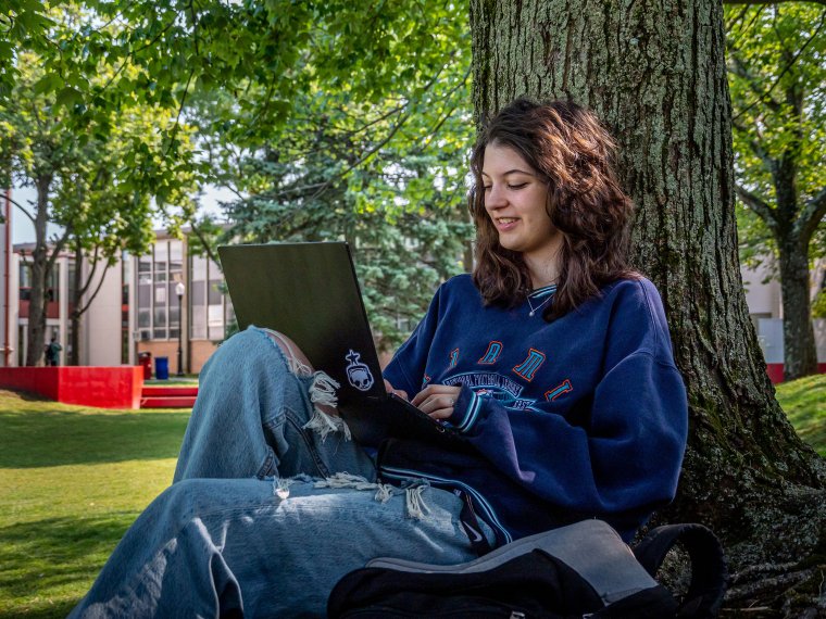 Student sitting under a tree, using their laptop.