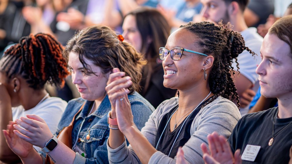 Students in a crowd smile and applaud.