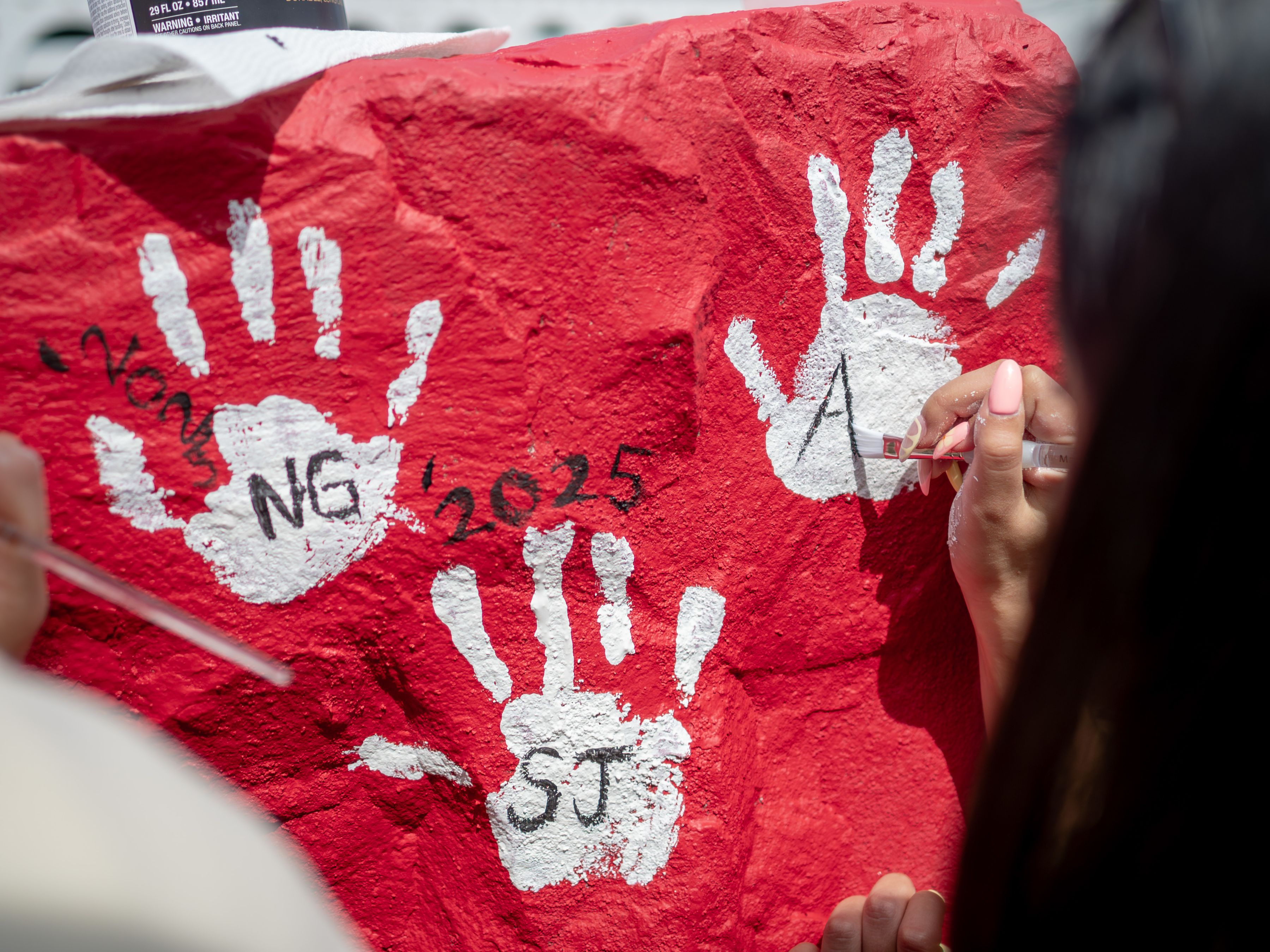 A photo of a red-painted rock with white handprints