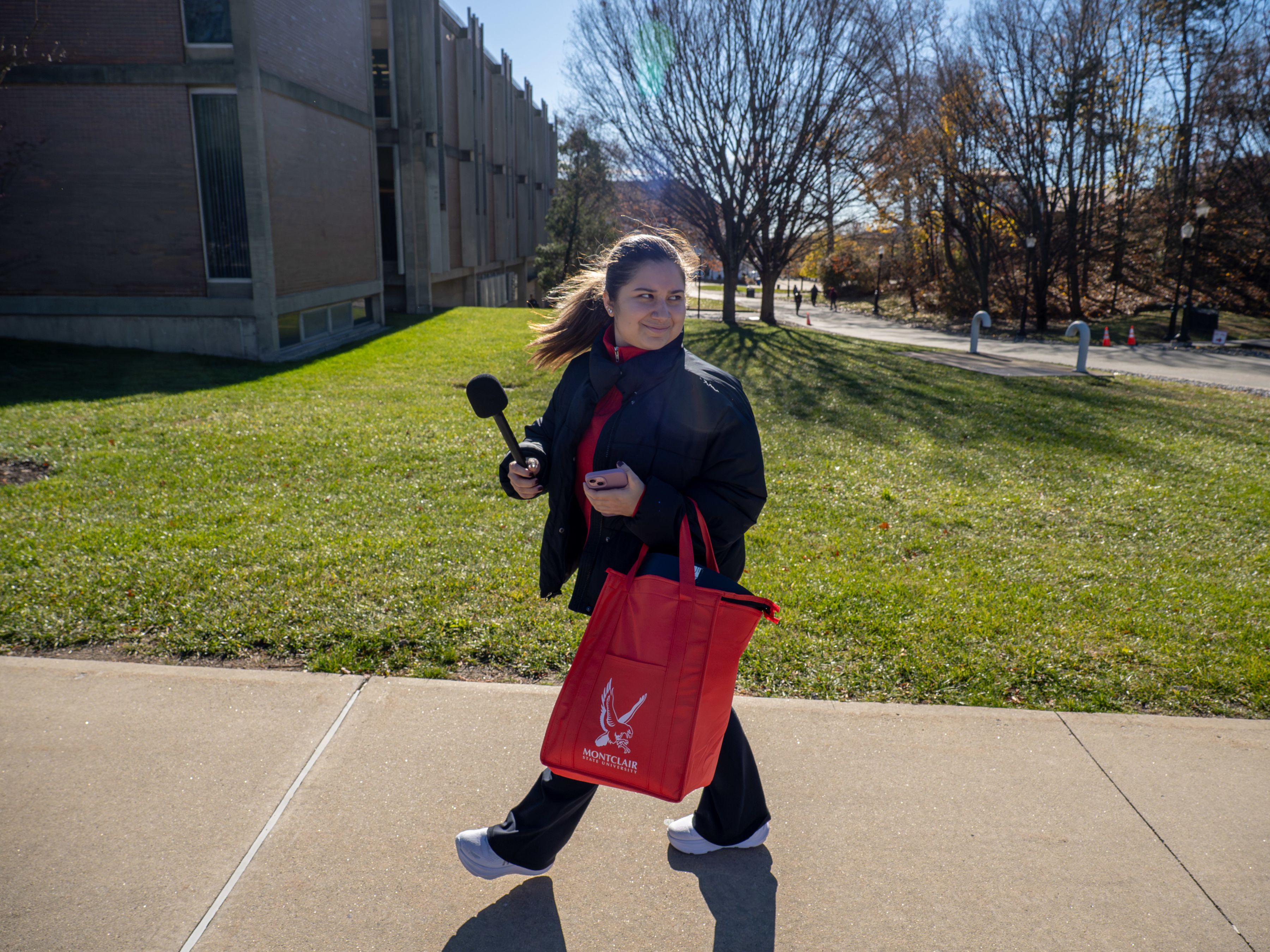 A social media ambassador walks down a pathway with a camera on a selfie stick between classes